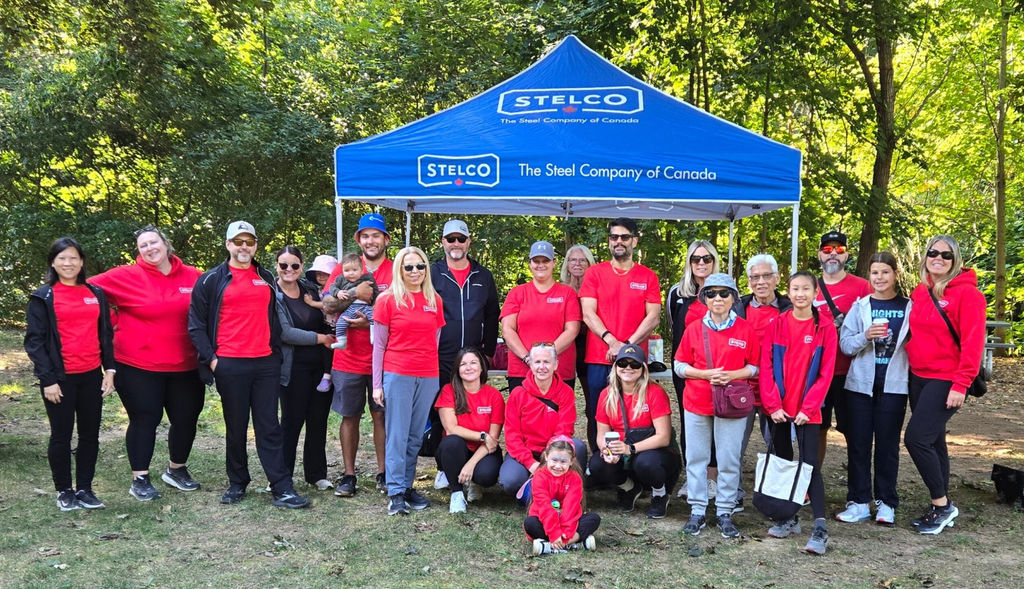 a group of people outdoors wearing red tee shirts and standing under a blue Stelco tent